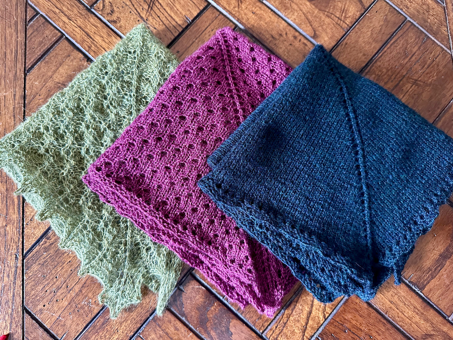 Three knitted shawls folded, on a wooden surface
