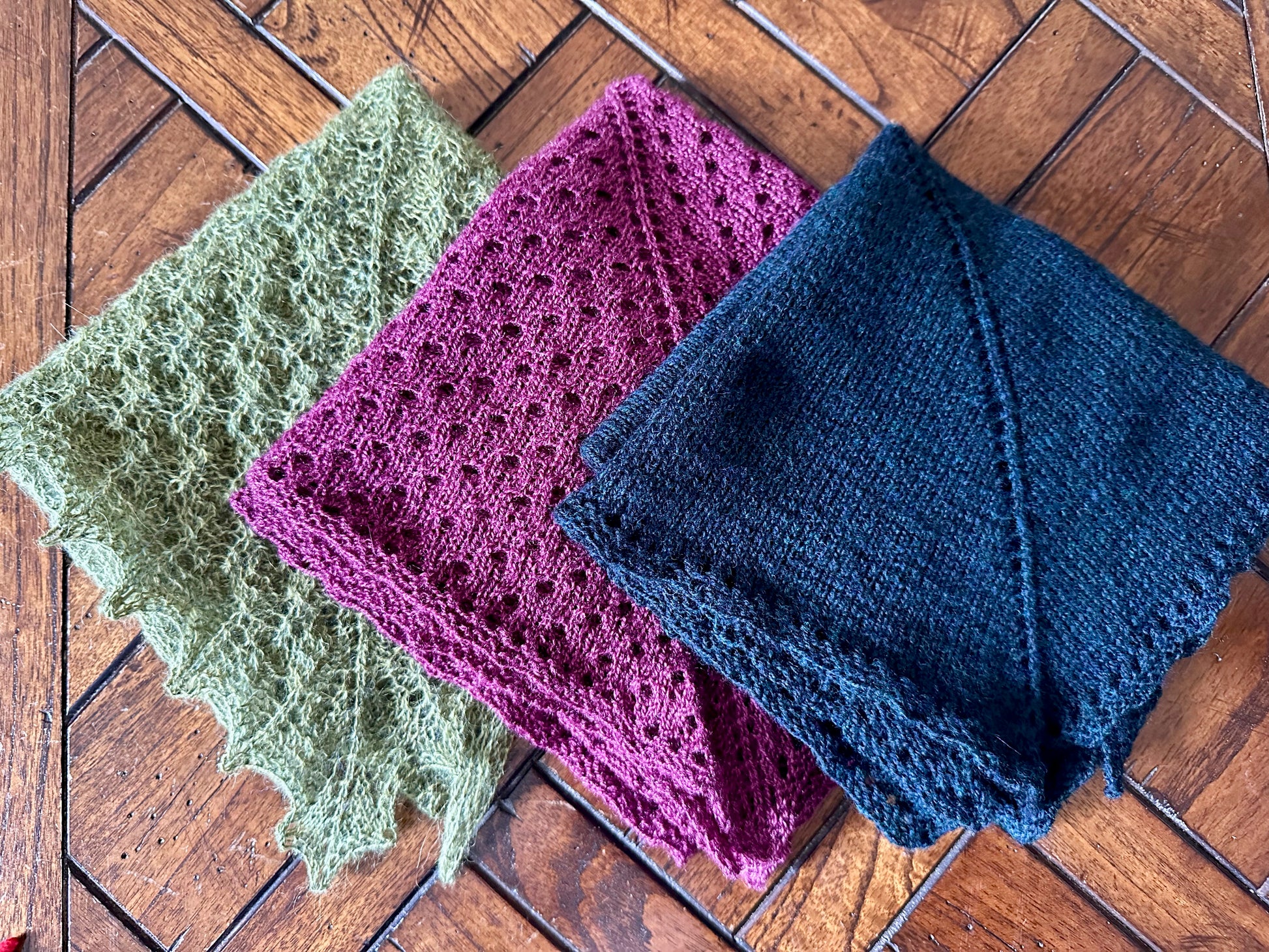 Three knitted shawls folded, on a wooden surface