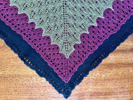 Three knitted shawls on a wooden surface